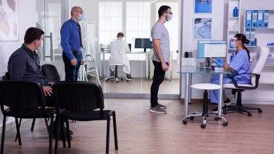 young man checking appointment respecting social distancing hospital waiting room nurse looking computer wearing face mask against covid 19 482257 2003